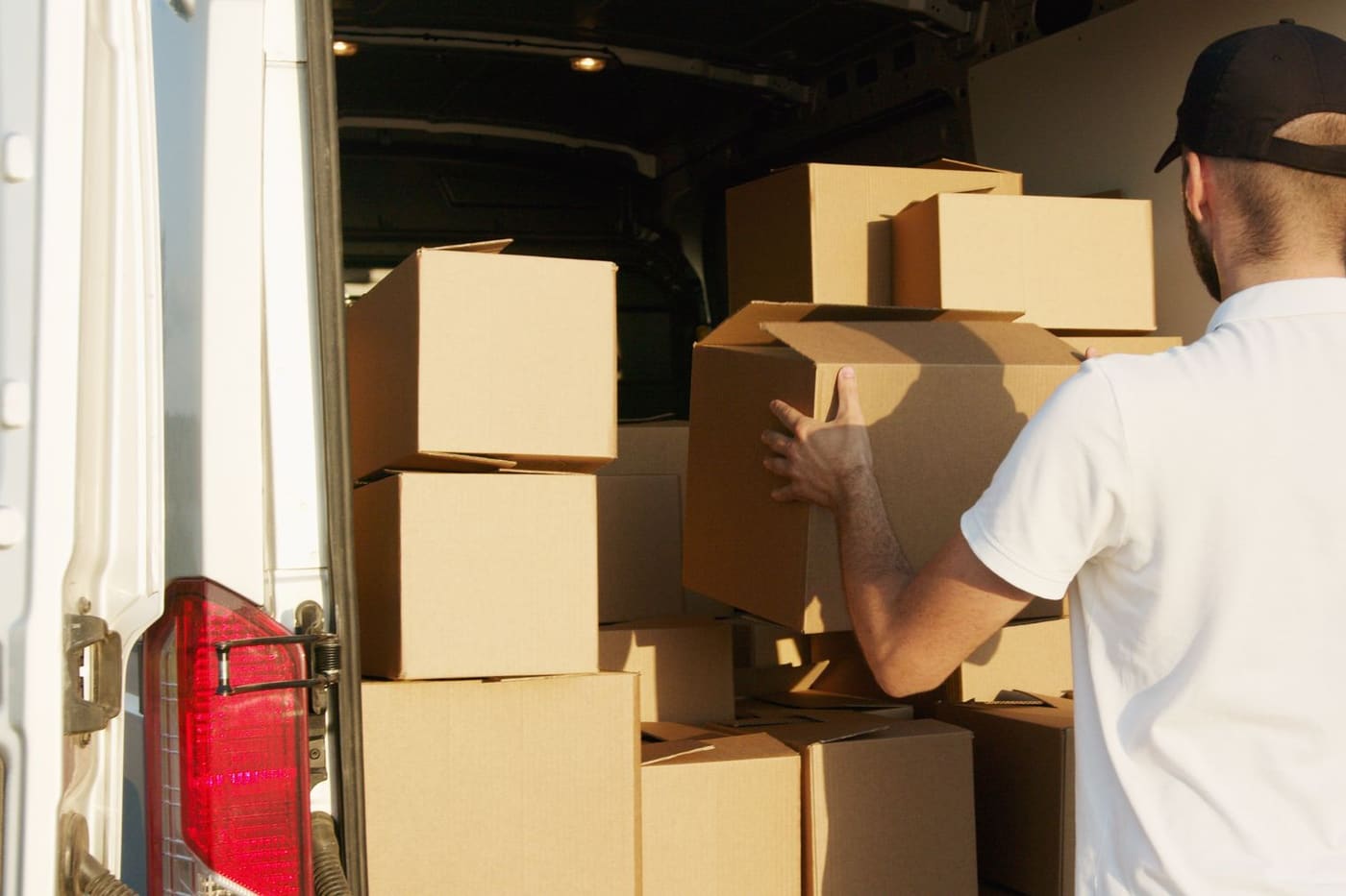 A porter stacking packed cardboard boxes into the back of a removals van